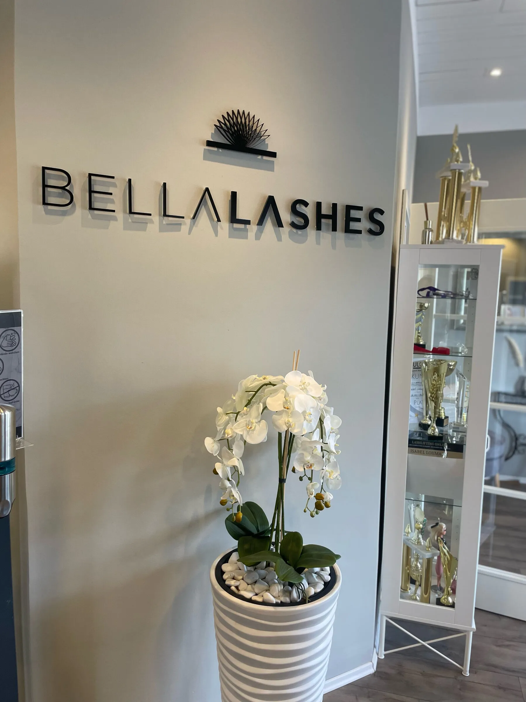 Empfang mit dem Bellalashes-Schriftzug an der Wand und einer weißen Orchidee